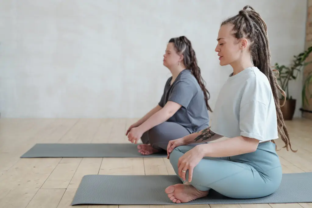 Two women sitting cross-legged on yoga mats during a stretching session