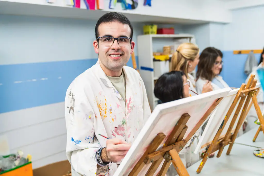 Smiling young man painting at an easel in an art class