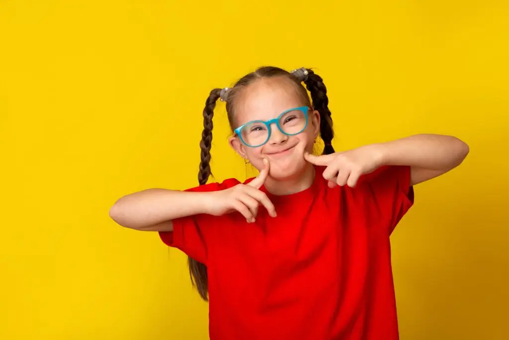 Smiling girl with pigtails and blue glasses in a red t-shirt against a yellow background