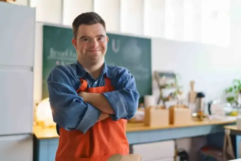 Micro enterprise support: smiling man in an orange apron standing in his café