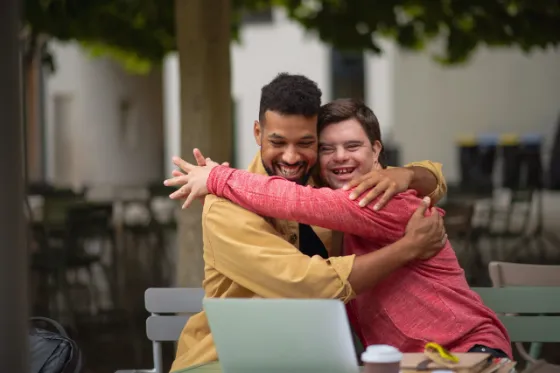 Two men sharing a hug and smiling at an outdoor café table